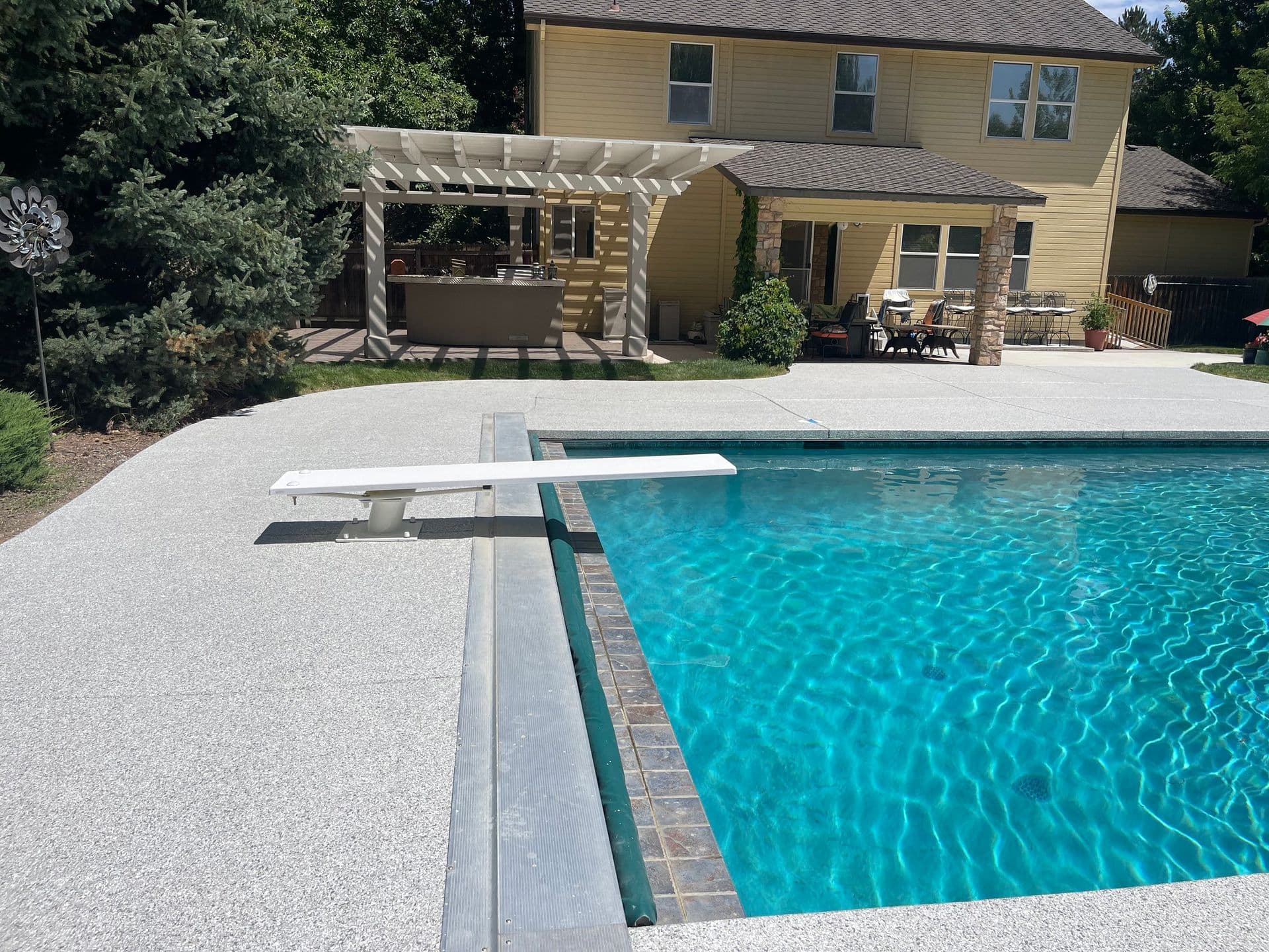 A gray-speckled polyurea concrete-coated pool deck around a pool with a diving board.
