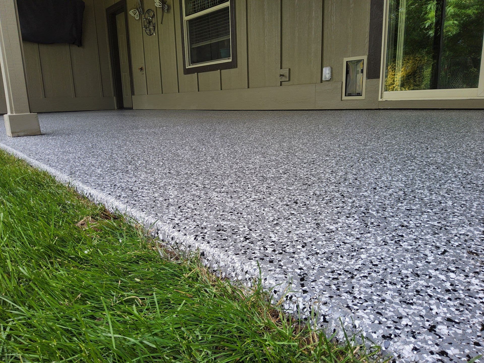 A close up of a gray, white, and black speckled concrete coated patio next to a lawn.