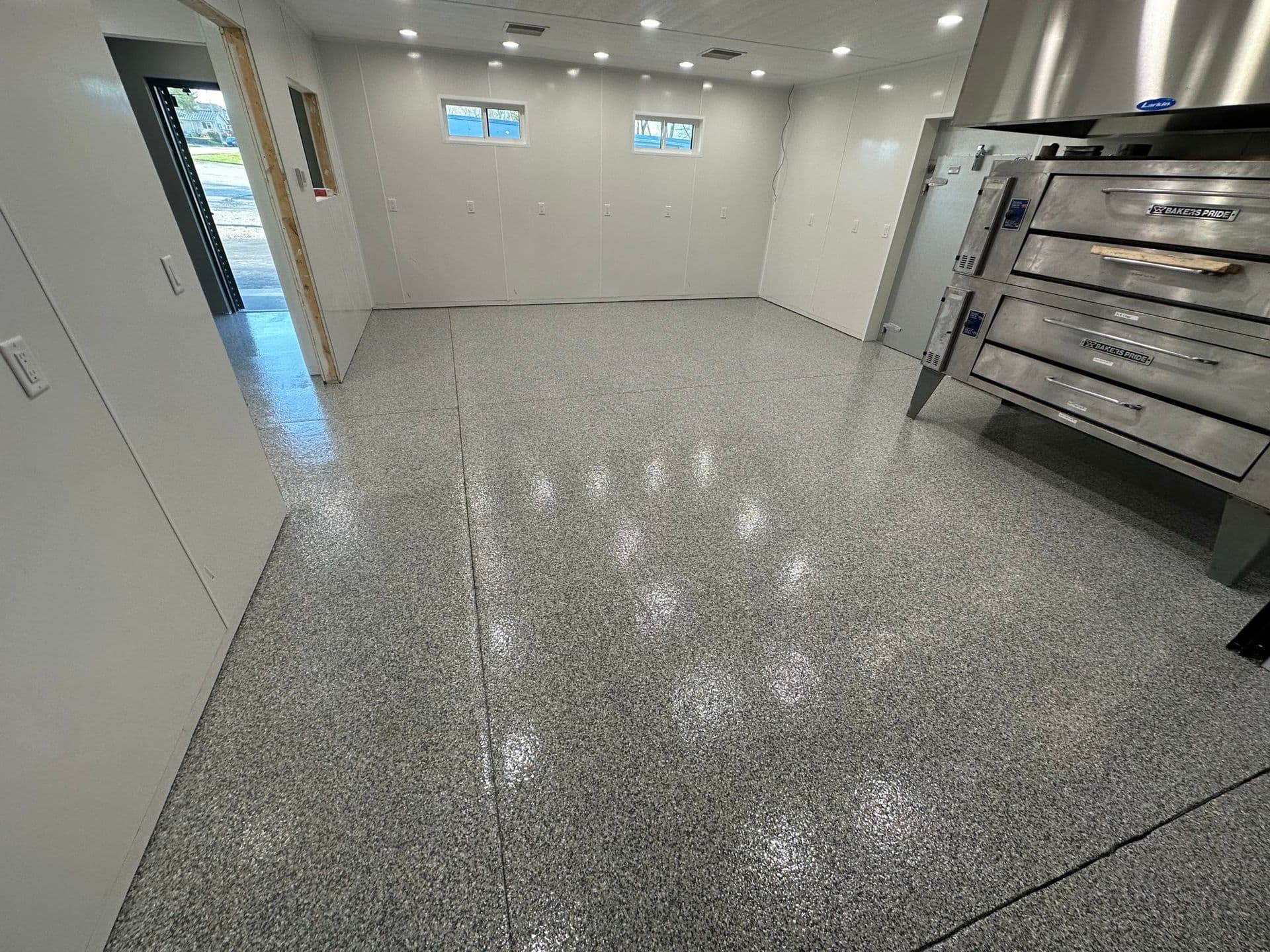 A commercial kitchen with a gray Penntek coated floor. A commercial pizza oven is visible off to the right side.